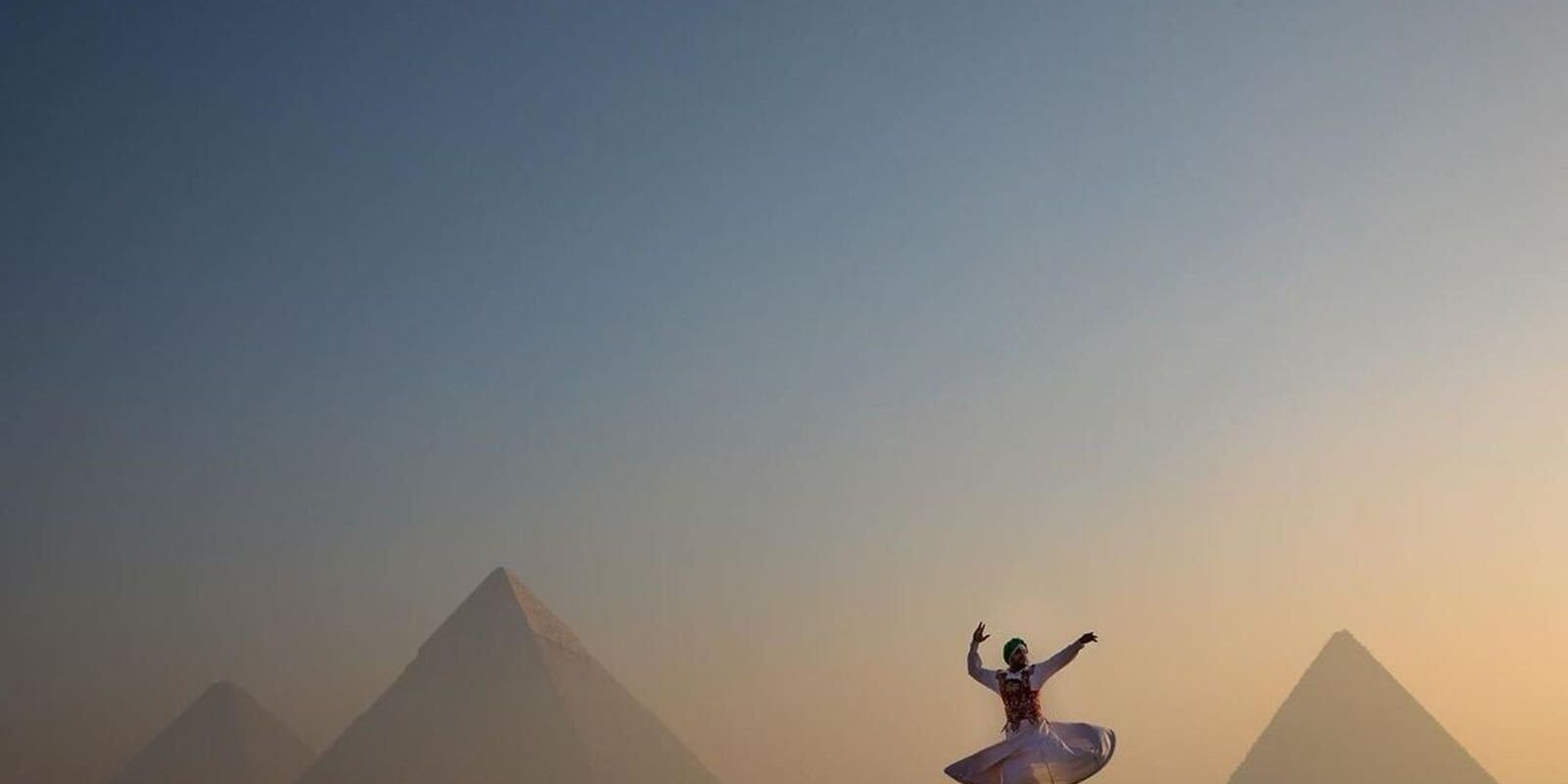 Giza Pyramids1 A woman in a white dress dances joyfully in front of the pyramids, showcasing the beauty of Egypt holiday experiences.