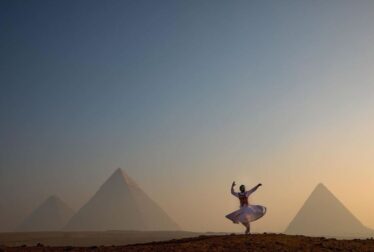A woman in a white dress dances joyfully in front of the pyramids, showcasing the beauty of Egypt holiday experiences.