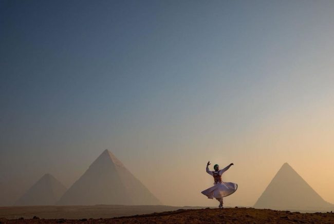 A woman in a white dress dances joyfully in front of the pyramids, showcasing the beauty of Egypt holiday experiences.