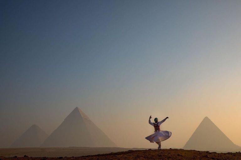 A woman in a white dress dances joyfully in front of the pyramids, showcasing the beauty of Egypt holiday experiences.